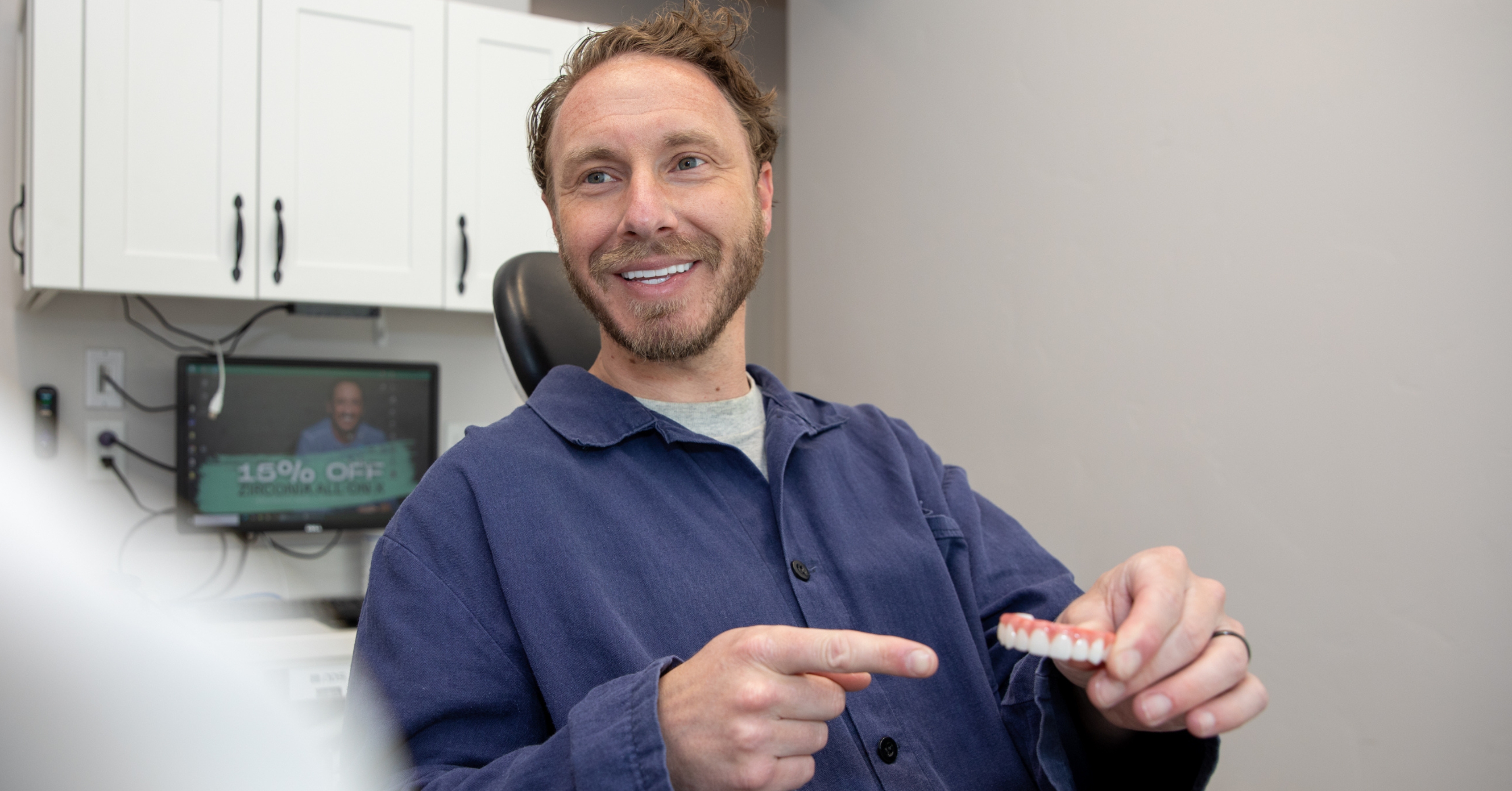Patient holding All-on-X zirconia teeth model while sitting in dental chair
