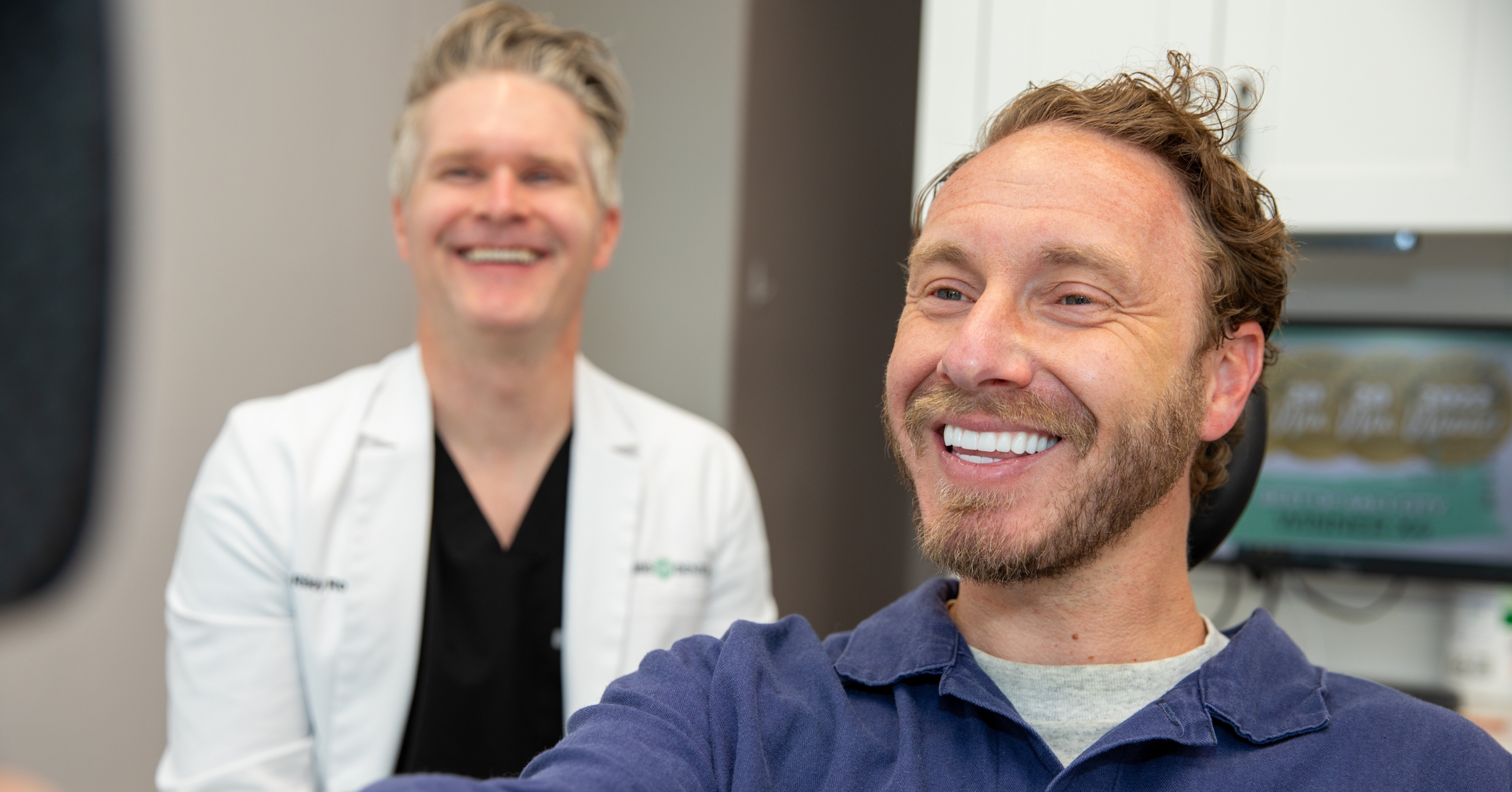 Patient sitting in dental chair smiling looking at his new teeth