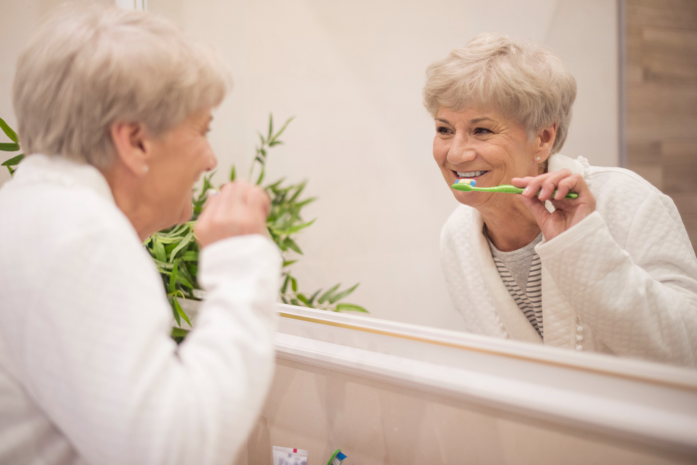 How to brush and clean dental implants older woman brushing teeth in the mirror.