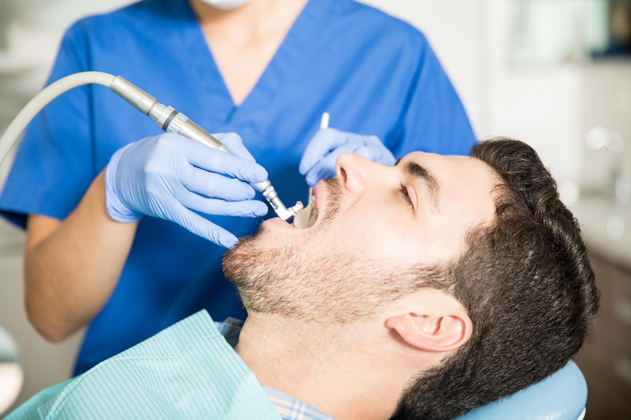 Male patient receiving dental cleaning treatment with professional hygienist at clinic.