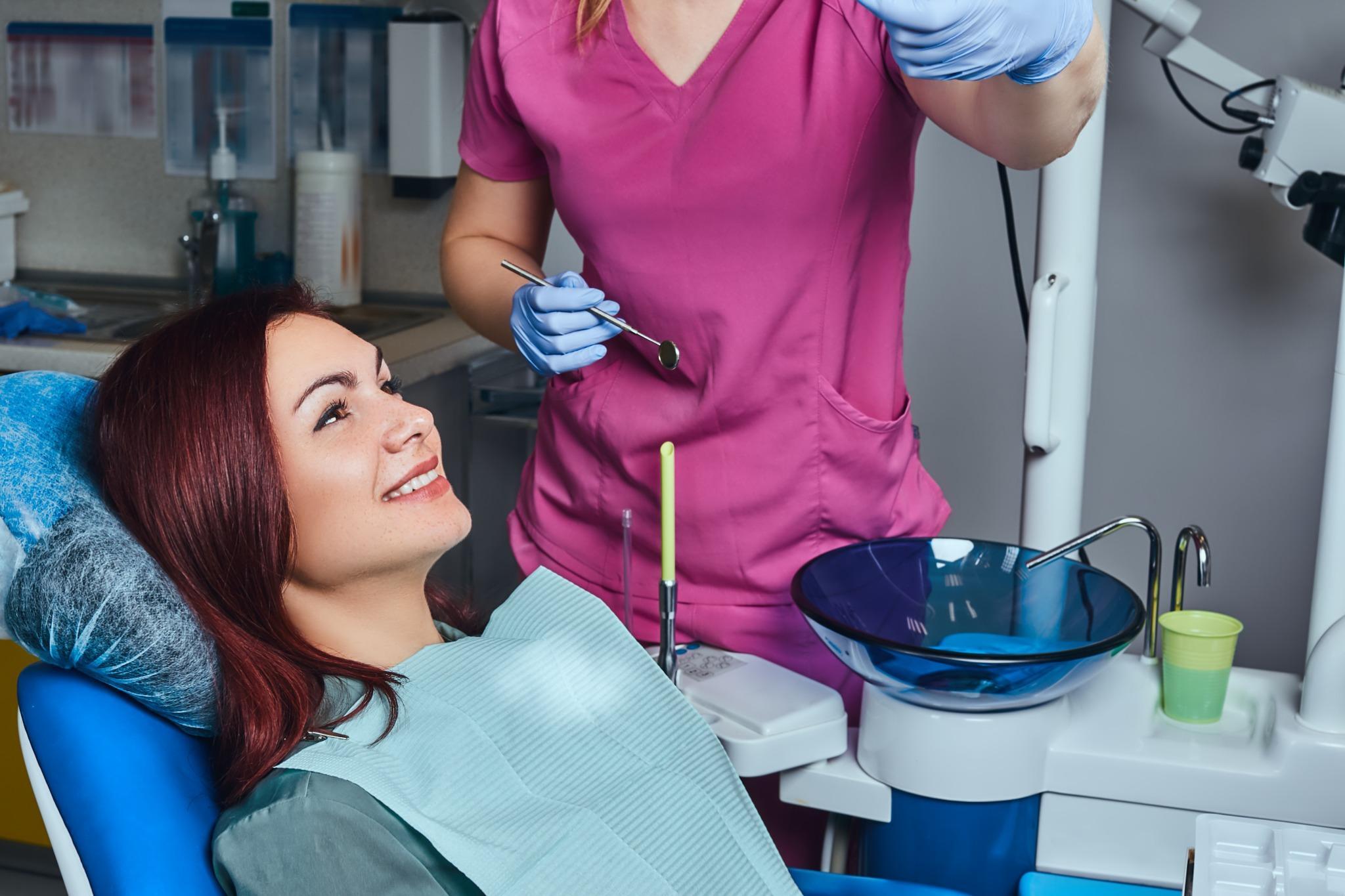 Smiling woman in dental chair preparing for routine dental cleaning appointment.