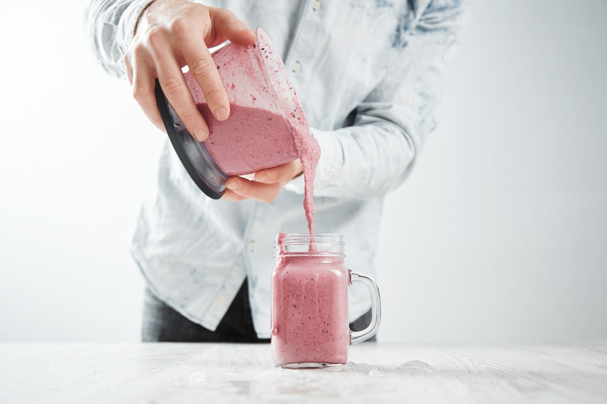 Person pouring a berry smoothie into a glass jar, showing soft foods to eat after oral surgery.